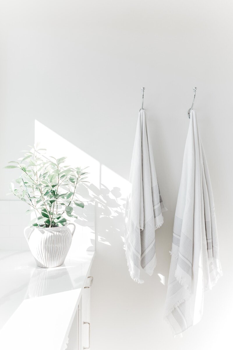 white walls, white countertop with white vase and green florals, two white bath towels hanging on separate hooks