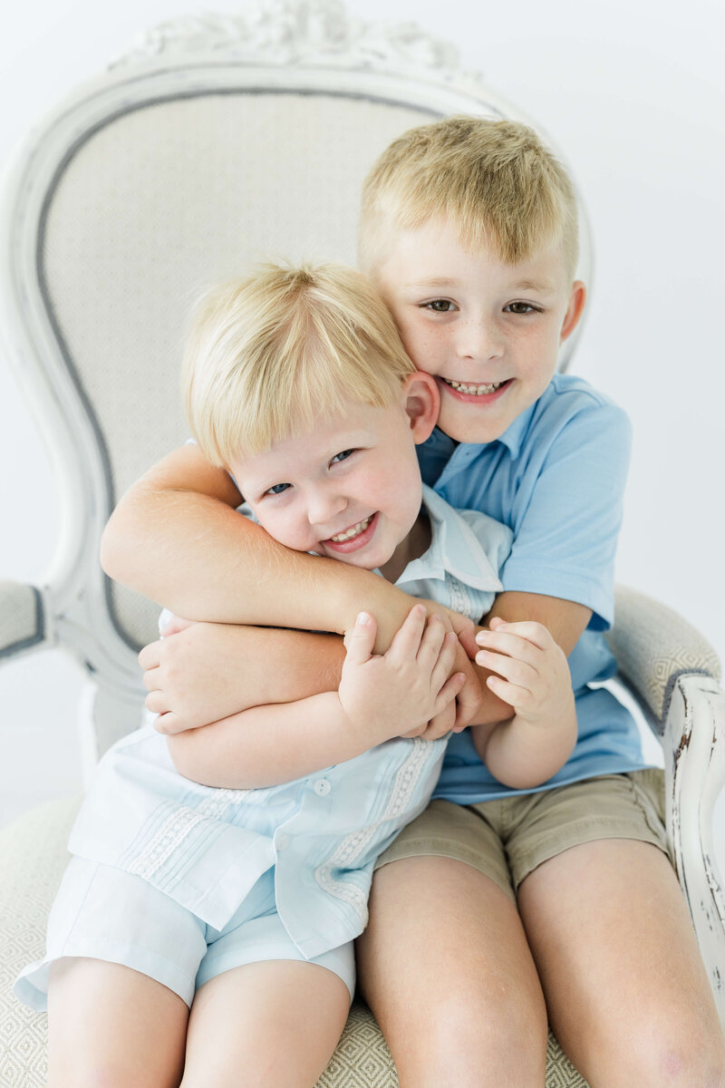 Siblings hugging sitting in chair for milestone photos in mini model rep program