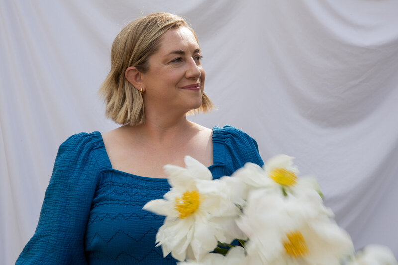 Graphic, web and branding designer Bess Brownlee smiles outside in a blue dress in Missoula, Montana.