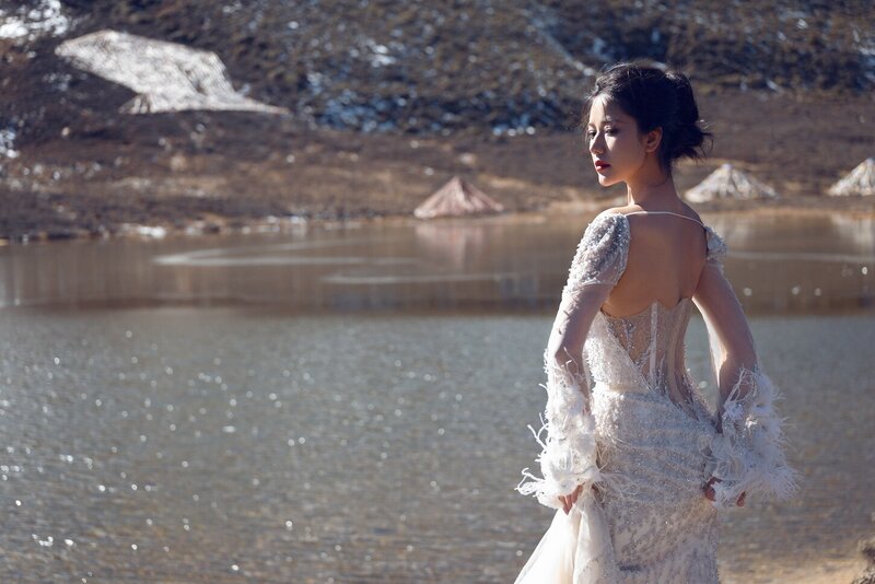 Dramatic shoot of a bride in a haute couture dress by an alpine lake in snow capped mountains.