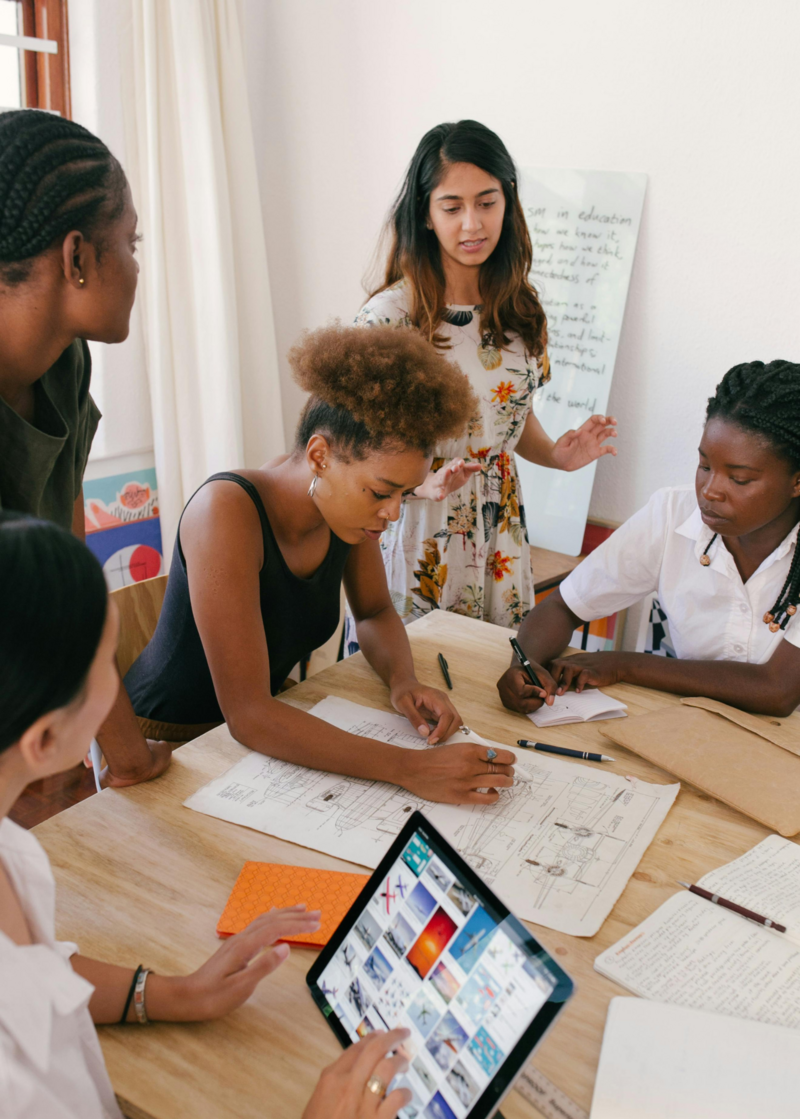 A group of mid-level to executive women engaged in a dynamic discussion at a conference, focusing on career coaching. The setting features a professional environment with a presentation in the background, highlighting collaboration and empowerment among women in leadership.