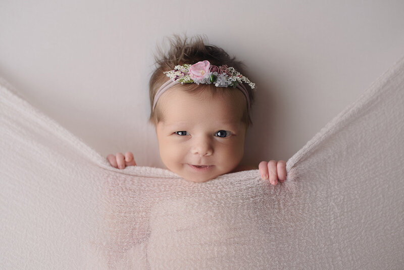 newborn baby girl in tucked in pose smiling