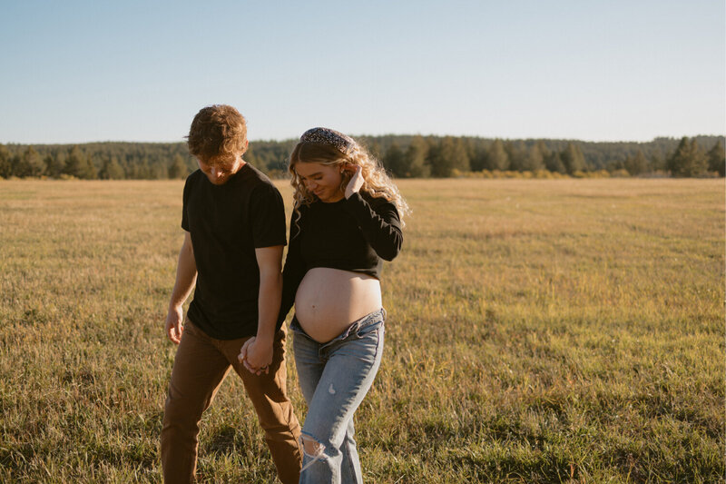 A husband and pregnant wife hold hands and walk candidly.