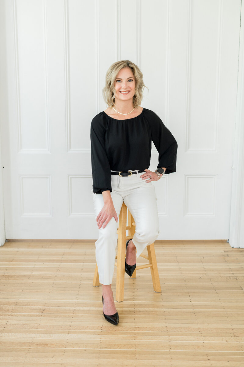 Contact Julie Ladimer, founder of Ladimer Law, sitting on a stool with a blue blouse and white jeans