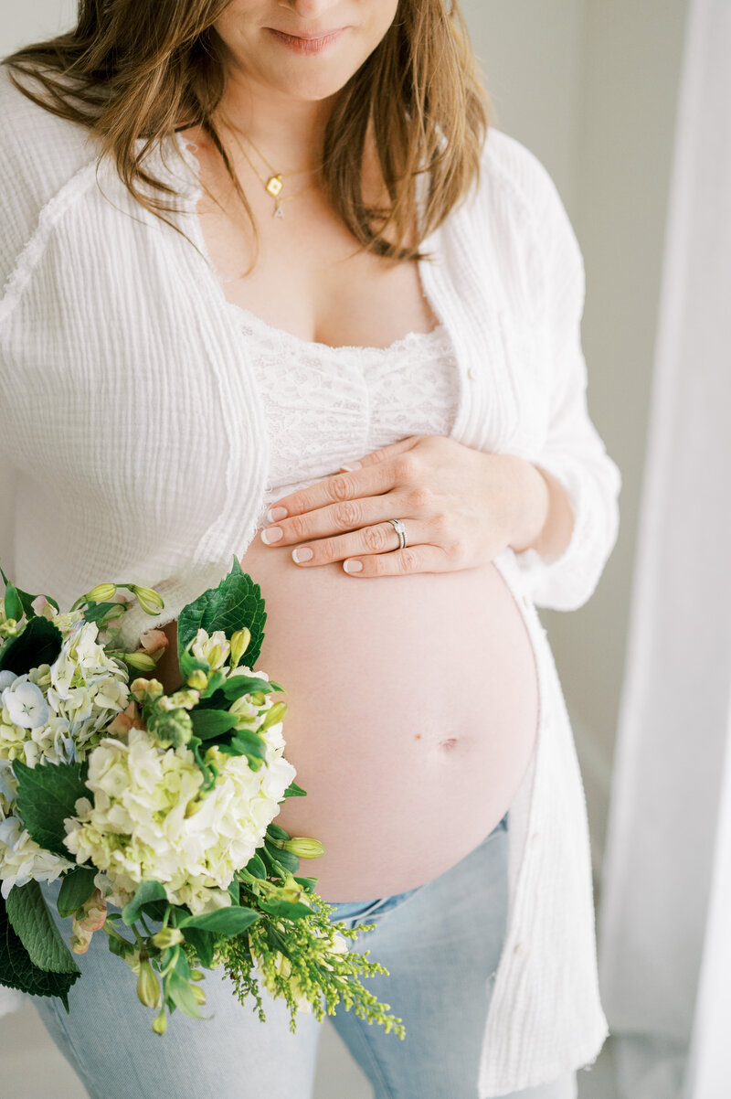 Expecting mother holds hand over exposed belly with florals during studio maternity session