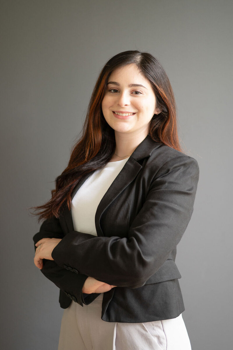 Isabella standing against gray background in white top and black blazer