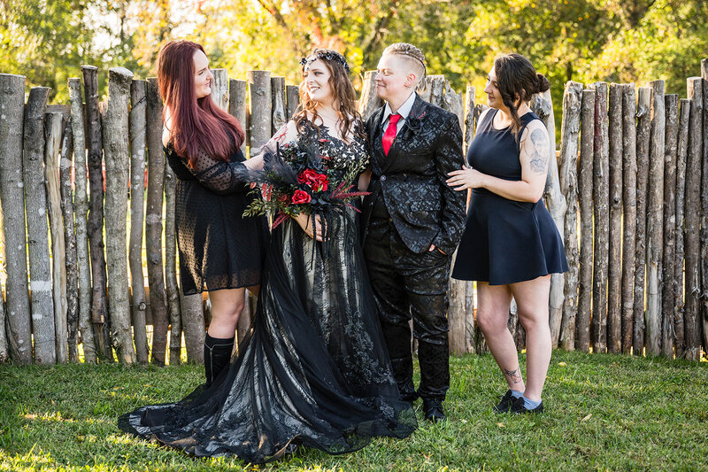 Two brides stand next to one another for a photo sandwiched between their respective persons of honor on their elopement day at an Airbnb in Roanoke, Virginia.