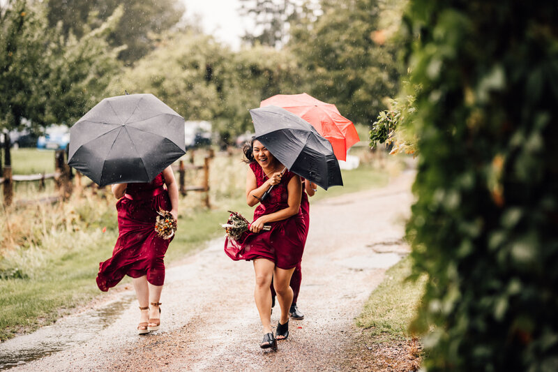Bridesmaids in red dresses laughing while carrying umbrellas to wedding ceremony