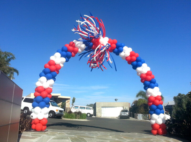 Arch of red, white, blue balloons set up in outdoor area