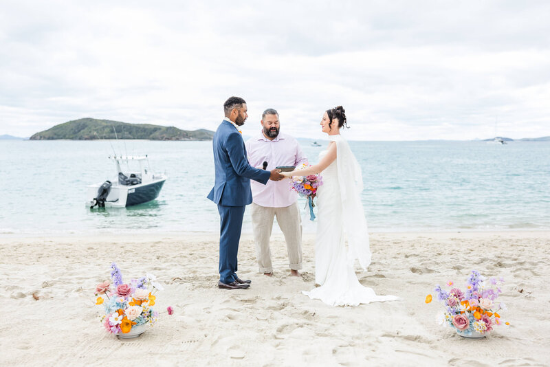 Bride and groom exchanging vows in front of the ocean. Gorgeous florals in the foreground. Location is Great Keppel Island, Queensland. Captured by Julie-Anne Photography.