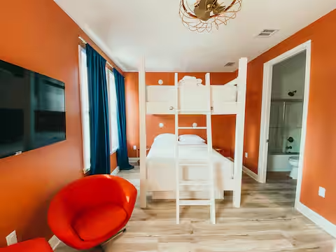Bold orange bedroom with queen-over-queen bunk beds and vintage flair at Groovy Shack, a vibrant vacation rental near Panama City Beach and 30A.