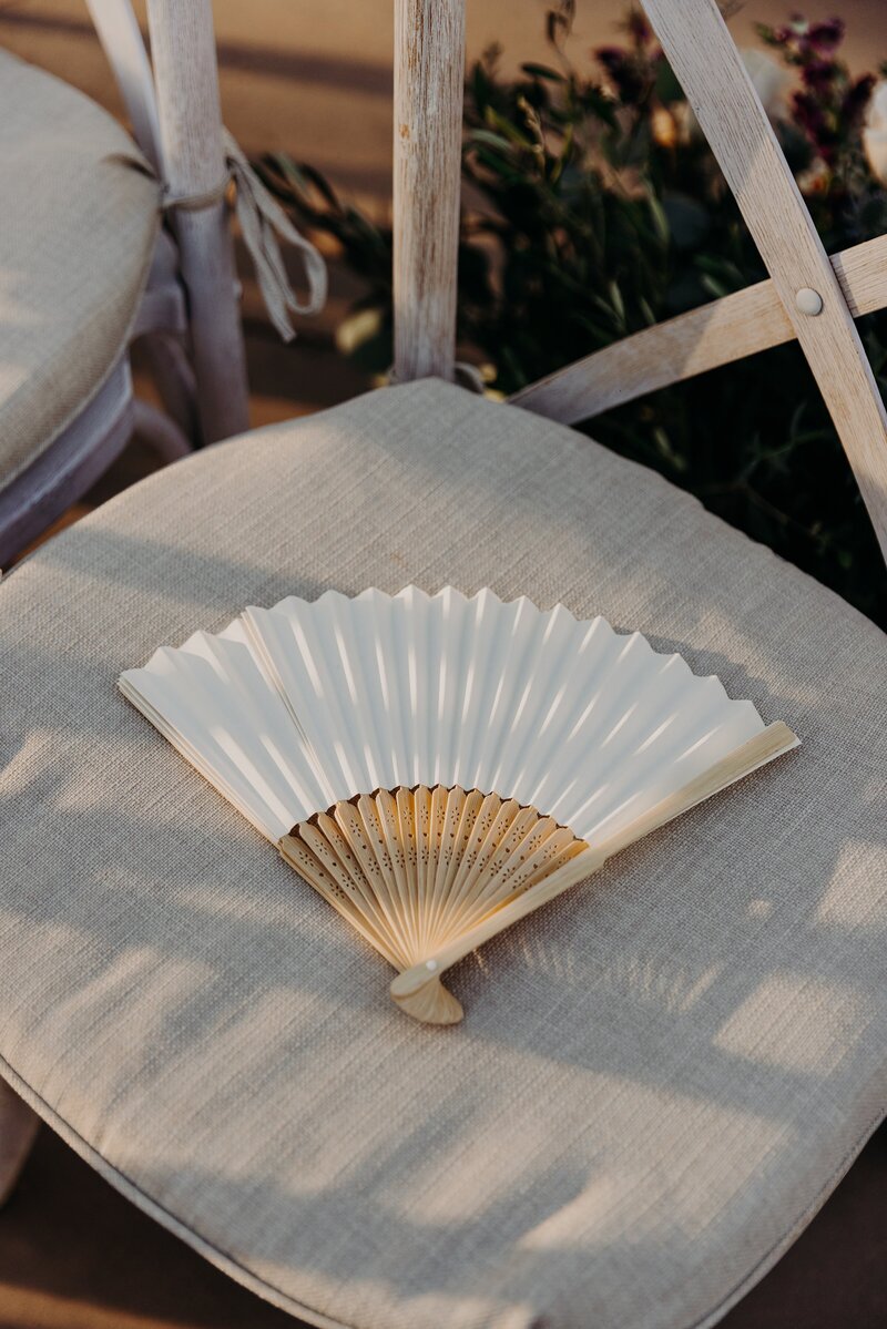 handheld fan open sitting on chair at wedding ceremony