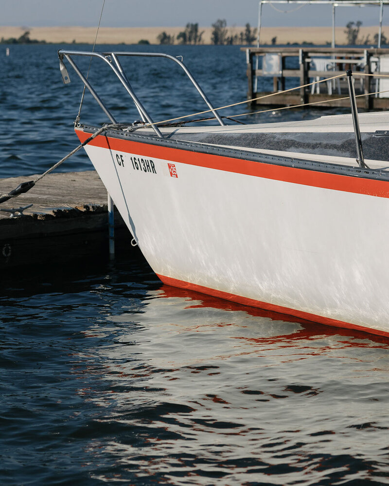 A white and red boat is moored to a wooden dock on a calm body of water.