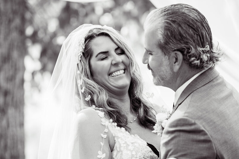 Bride laughing with her eyes closed as groom smiles at her.