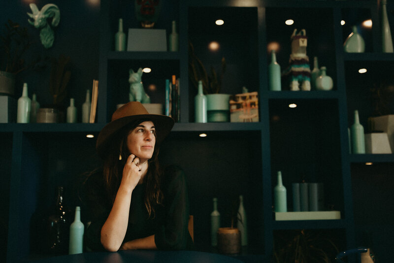 Portrait of Photography mentoring program graduate Laura  seated at table wearing hat