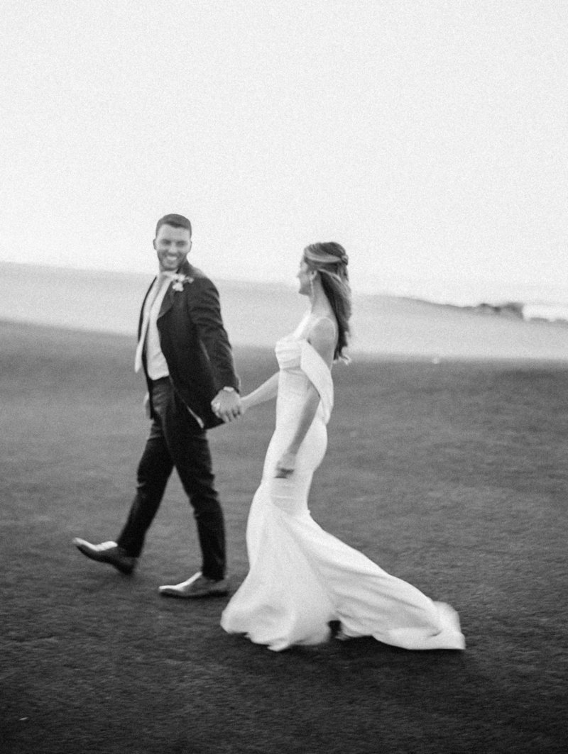 Black and white image of couple walking at 14th hole of Monterey Pennisula Golf Course at sunset with ocean and  cliffs in the back ground