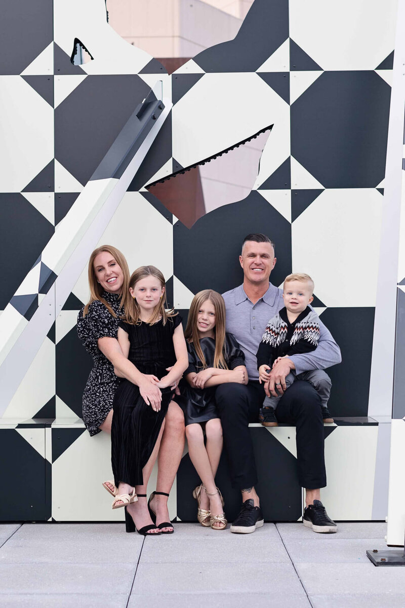 Family of five sitting in front of a black and white wall smiling
