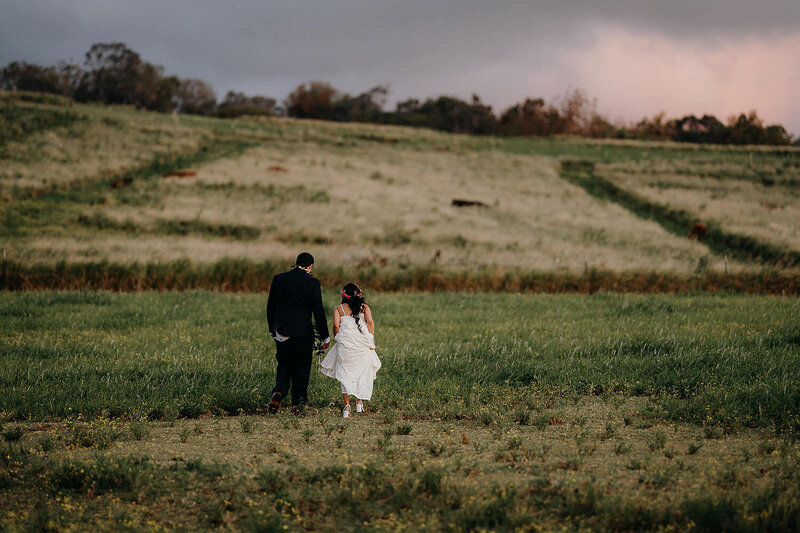 Couple walks away from camera in an open field in their suit and dress