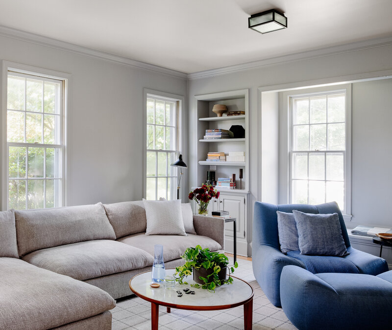 Interior decorators in Boston creates modern family room in old Hingham home featuring a blue chair and ottoman in a light grey room within an Italianate farmhouse.