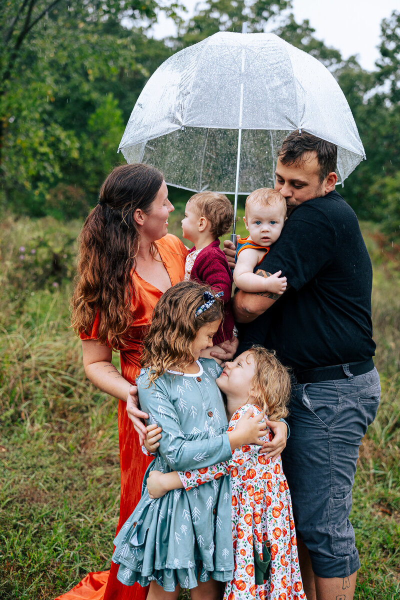 Family of six standing with am umbrella in the rain embracing in hugs in Farmington, Missouri. 