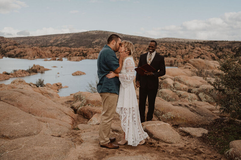 A bride and groom during their first kiss with their wedding parties standing on either side.