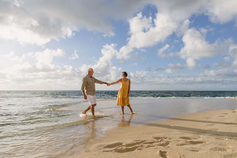 A man and woman hold hands along the beach of Honolulu.