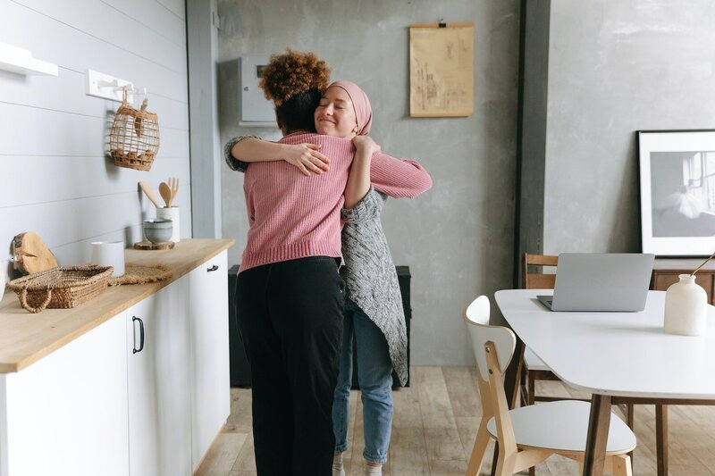 Woman in pink sweater giving cancer survivor a hug.
