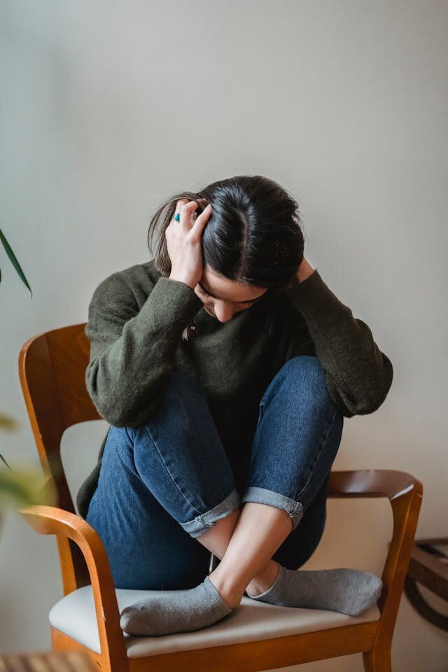 woman in chair covering her head with her hands