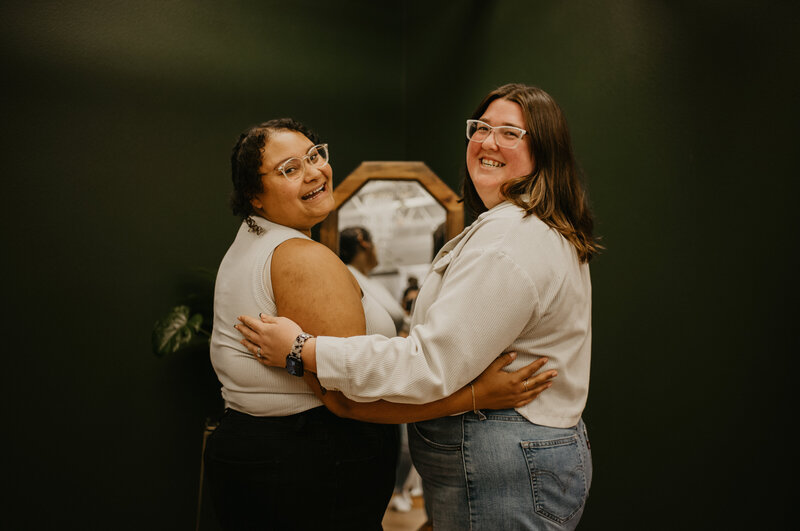 Ashley and Katelin in Studio Kalos in Corvallis, looking back at the camera with their arms around each other.