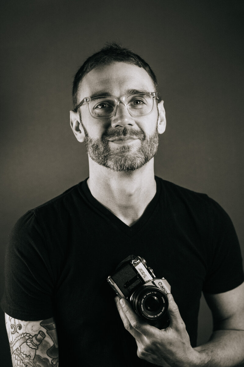 Black and white photograph of a photographer holding a canon film camera.