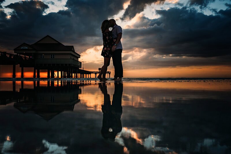 engaged couple on clearwater beach by pier during sunset with reflection