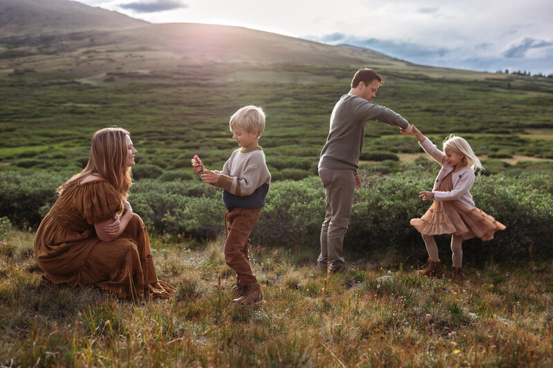Family with two young children in the mountains of Colorado. Dad is twirling little girl and boy is bringing his mom a flower.