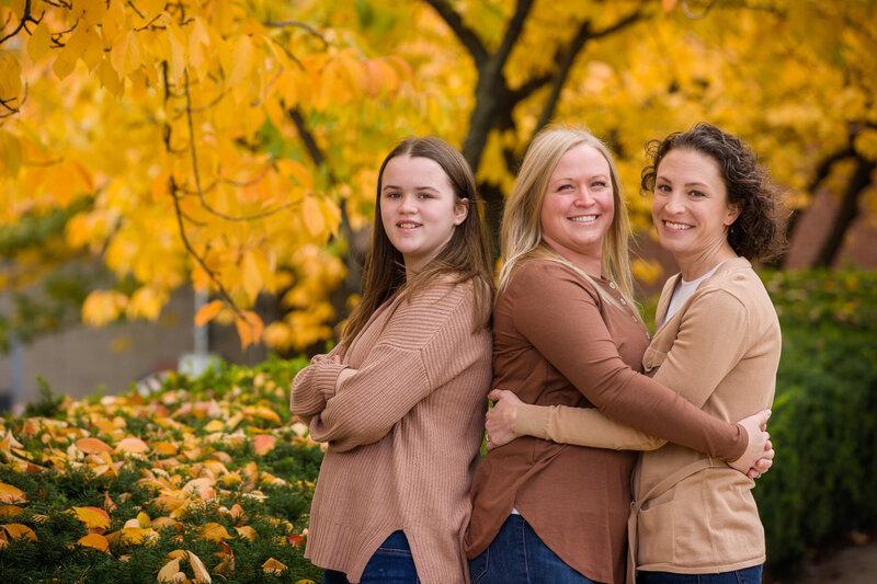 A same-sex couple smiling lovingly alongside their young daughter during a heartfelt mini session in Phoenixville.