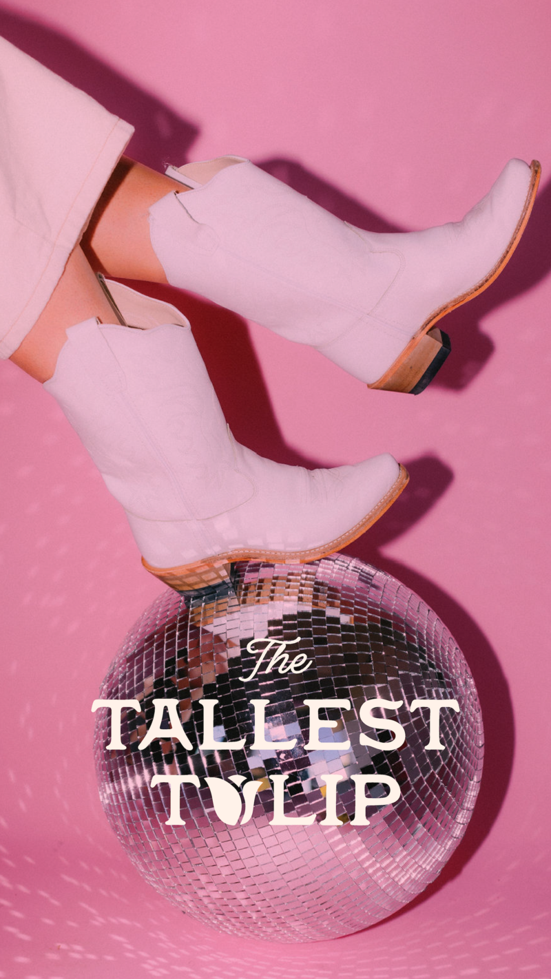 White cowgirl boots on a disco ball on a bright pink background