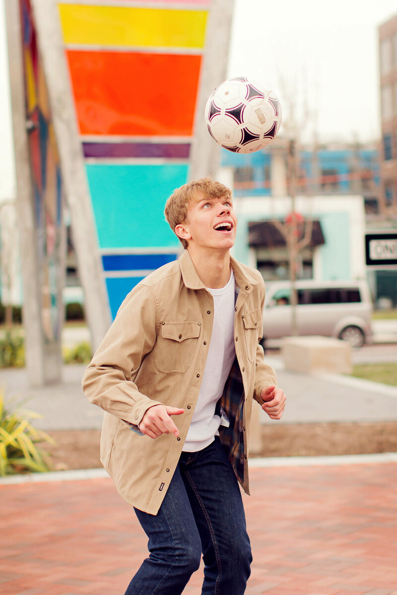 Fun senior playing with a soccer ball at the colorful scene of Carmel Arts and Design District.