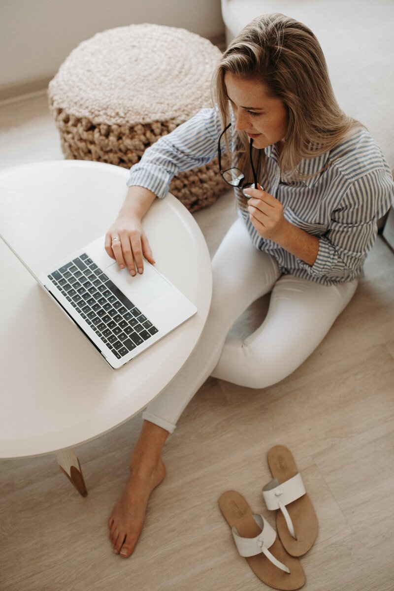 woman holding glasses looking at laptop