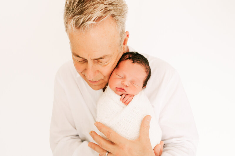 dad holding newborn baby on his shoulder in white newborn photography studio in Springfield MO