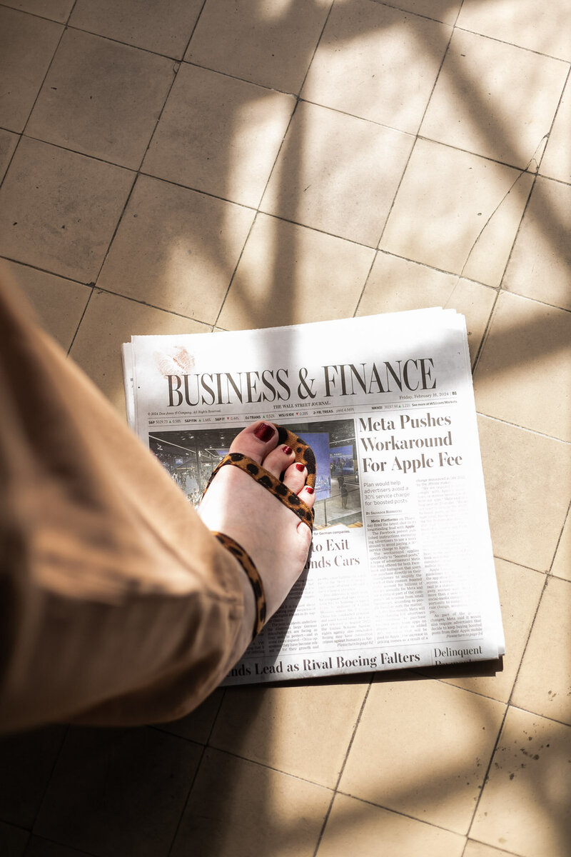 Business and Finance Newspaper with a cheetah print heel on tile floor with light dancing, by Ashleigh Henry, life coach for millionaire women in business, seeking intentional wellness practices for their stress-filled lives. 