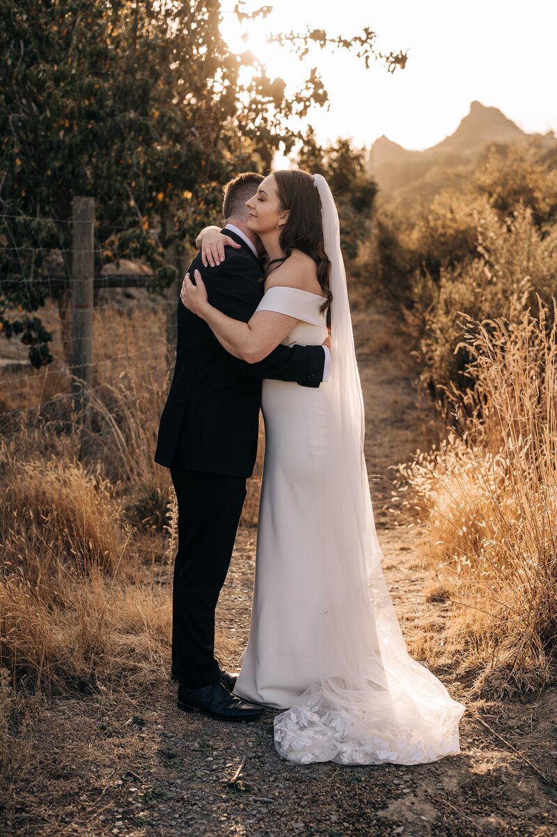 a groom hugs the bride in the golden sunset at the winehouse in queenstown