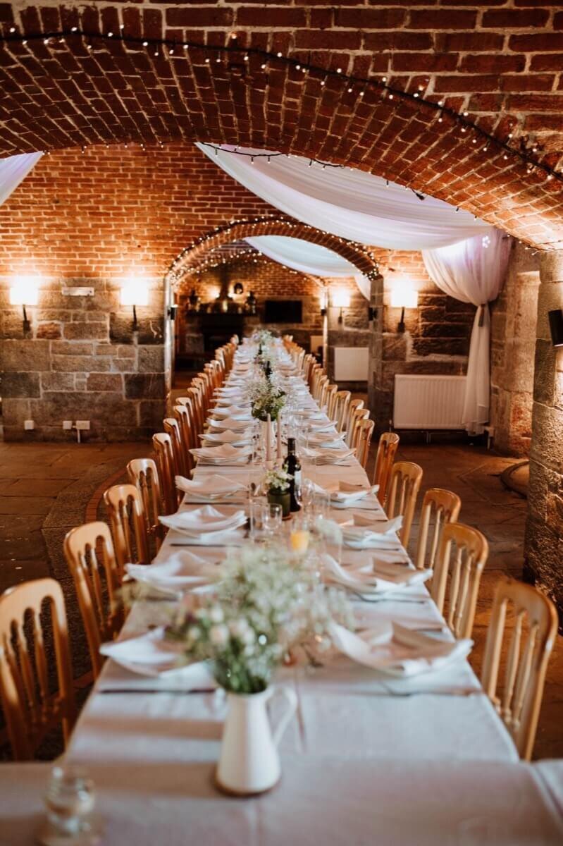 A long table set up in the fort halls with flowers wine and wooden chairs