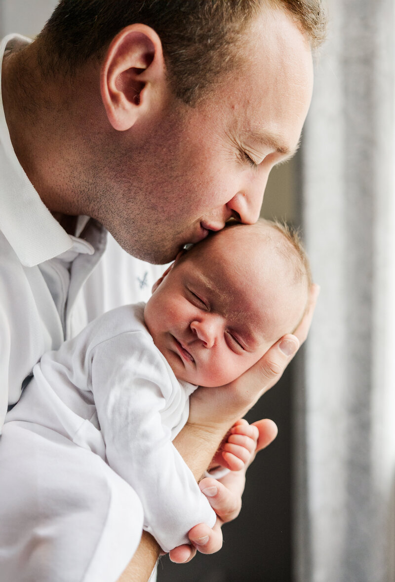 Newborn baby being kissed by his father on the head during a photoshoot