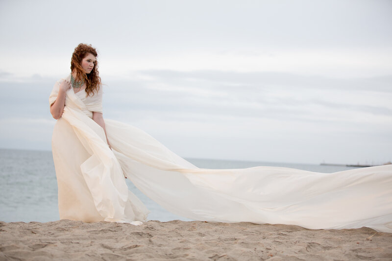 Beautiful red haired woman standing on beach wearing long white dress