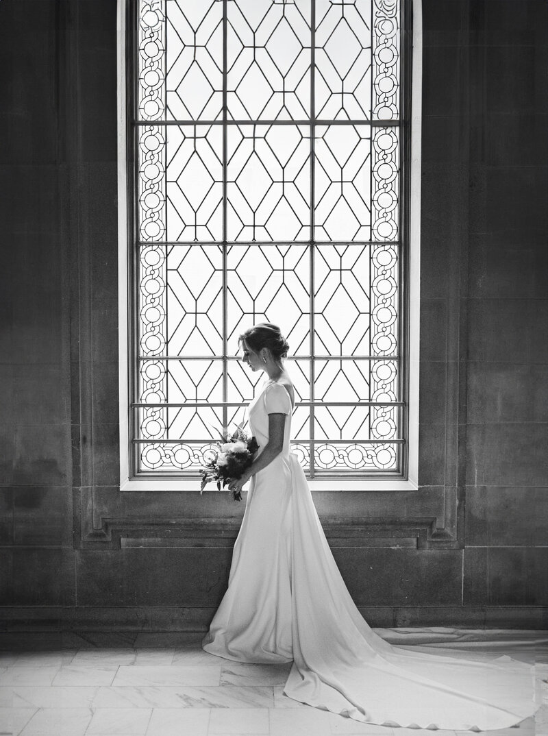 A serene bride stands by a stunning stained glass window, captured by Tiffany Longeway Photography. This image highlights the elegance and beauty of San Francisco wedding photography.