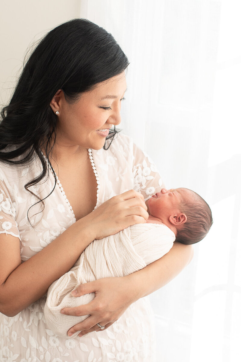 Mother smiling at newborn son, in white