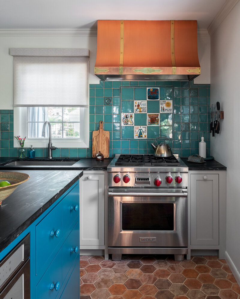colorful kitchen with stainless stove top, bright orange range hood and backsplash teal tiles