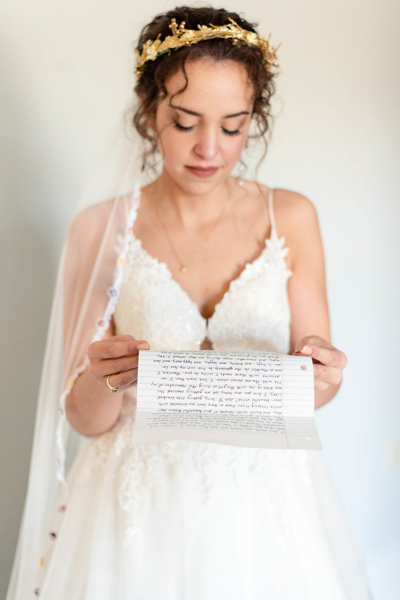 A bride looks down as she reads a letter from her groom on their wedding day.