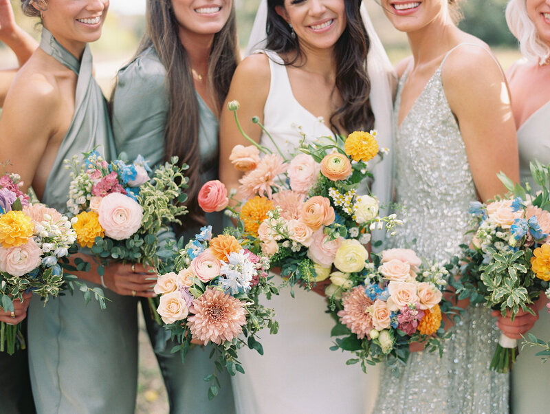 Close up of bride and her bridesmaids in green dresses holding colorful bouquets