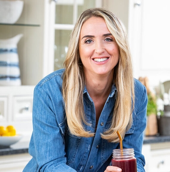 Charlotte Grand, founder of Menopause.Rescripted, smiling in the kitchen holding a smoothie