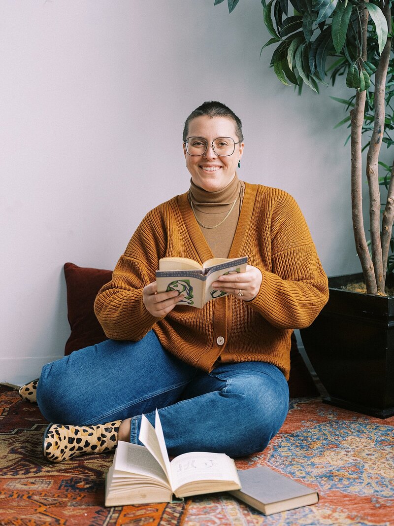 An SEO copywriter sits on a vintage carpet holding a book open.