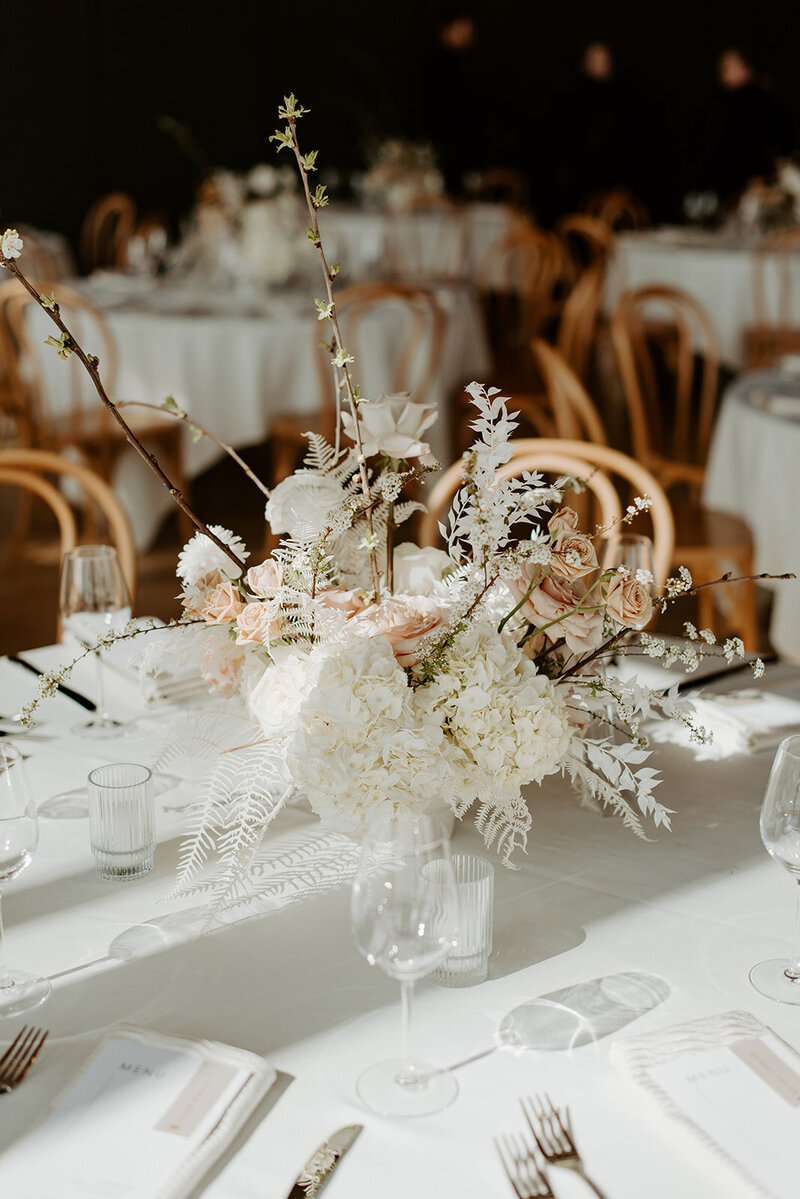 Close-up of modern floral centerpiece with white hydrangea, beige garden roses, and bleached fern in a lucite vase at Jenay and Daniel’s wedding, by Summer Robbins Flowers in Central Oregon